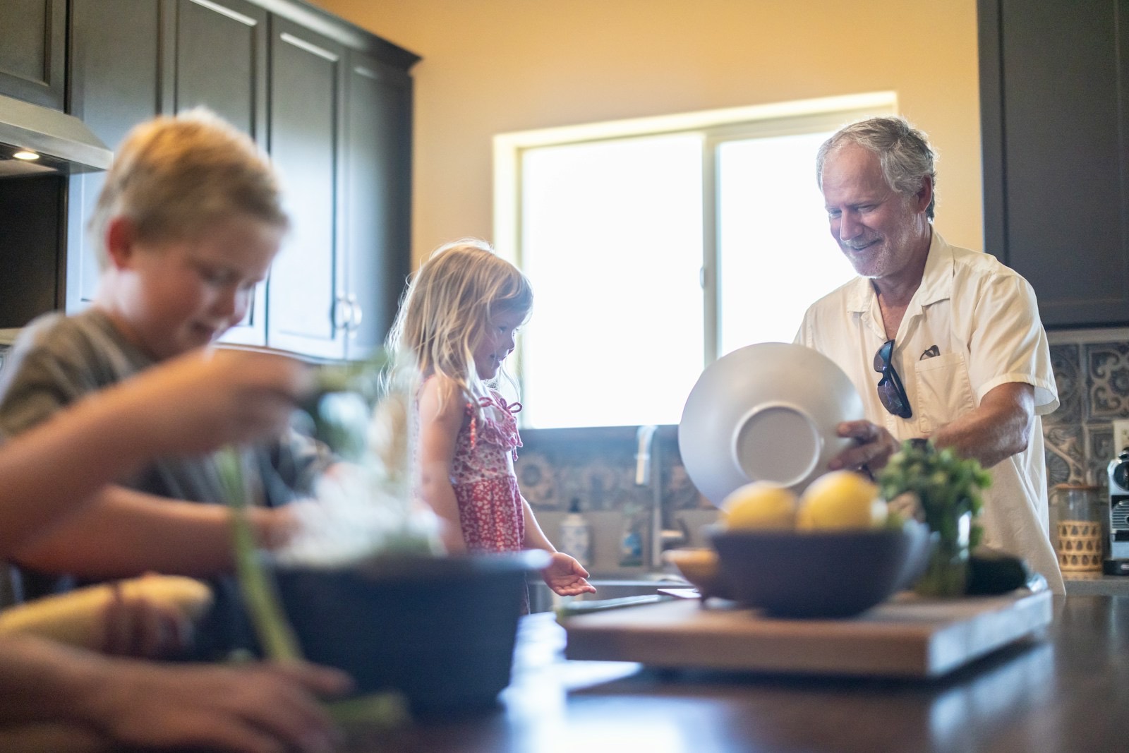 Een opa en twee kleinkinderen maken samen eten klaar in een keuken vol avondlicht