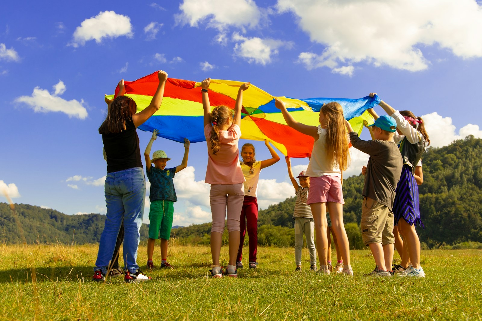 Kinderen tillen samen een kleurige parachute de lucht in op een zonnig grasveld